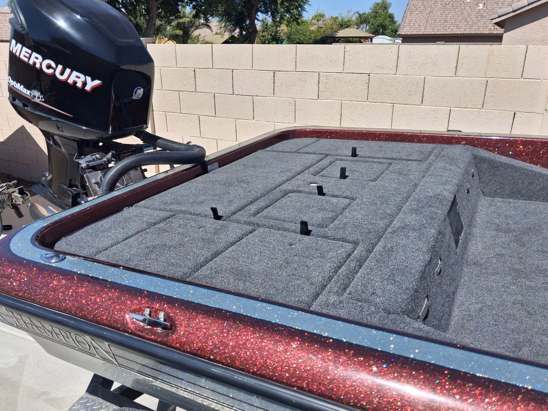 Rear deck of a burgundy metalflake Champion bass boat with newly installed gray marine carpet, rod straps and hatch lids cut in