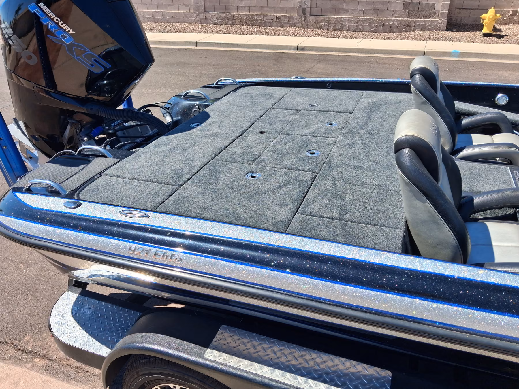 Rear deck and seats of a blue metalflake bass boat with fresh gray carpet, behind a Mercury Pro XS outboard