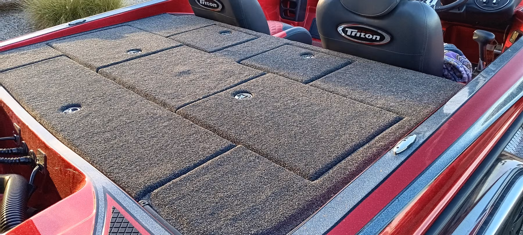 Close view of a red Triton bass boat rear deck showing individually carpeted hatch lids with recessed latches