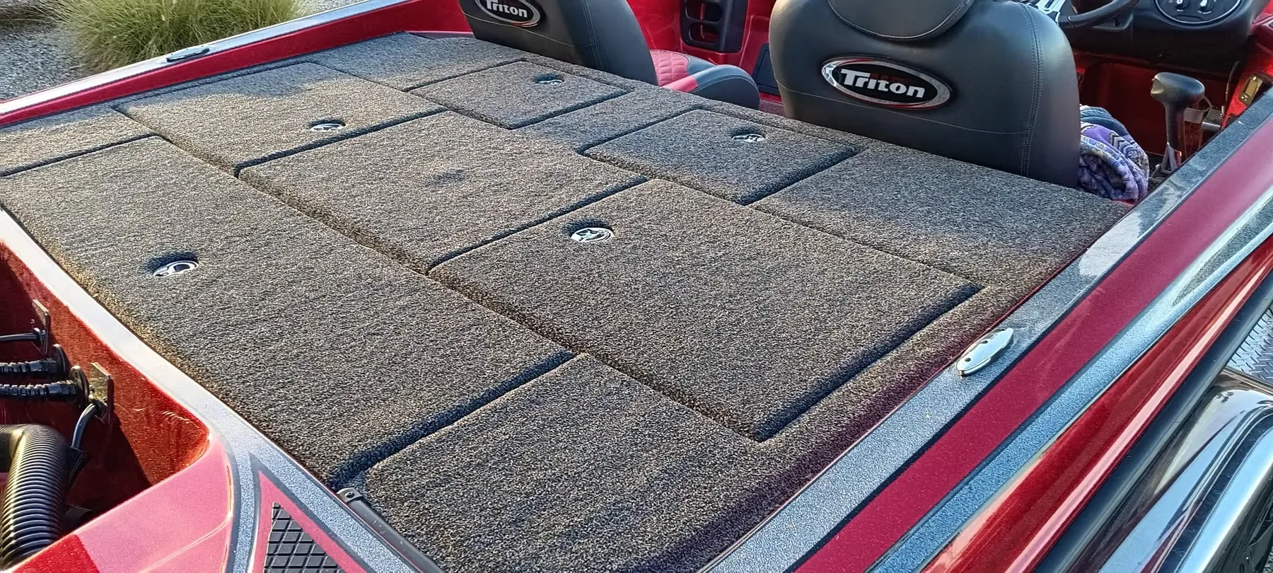 Close view of a red Triton bass boat rear deck showing individually carpeted hatch lids with recessed latches
